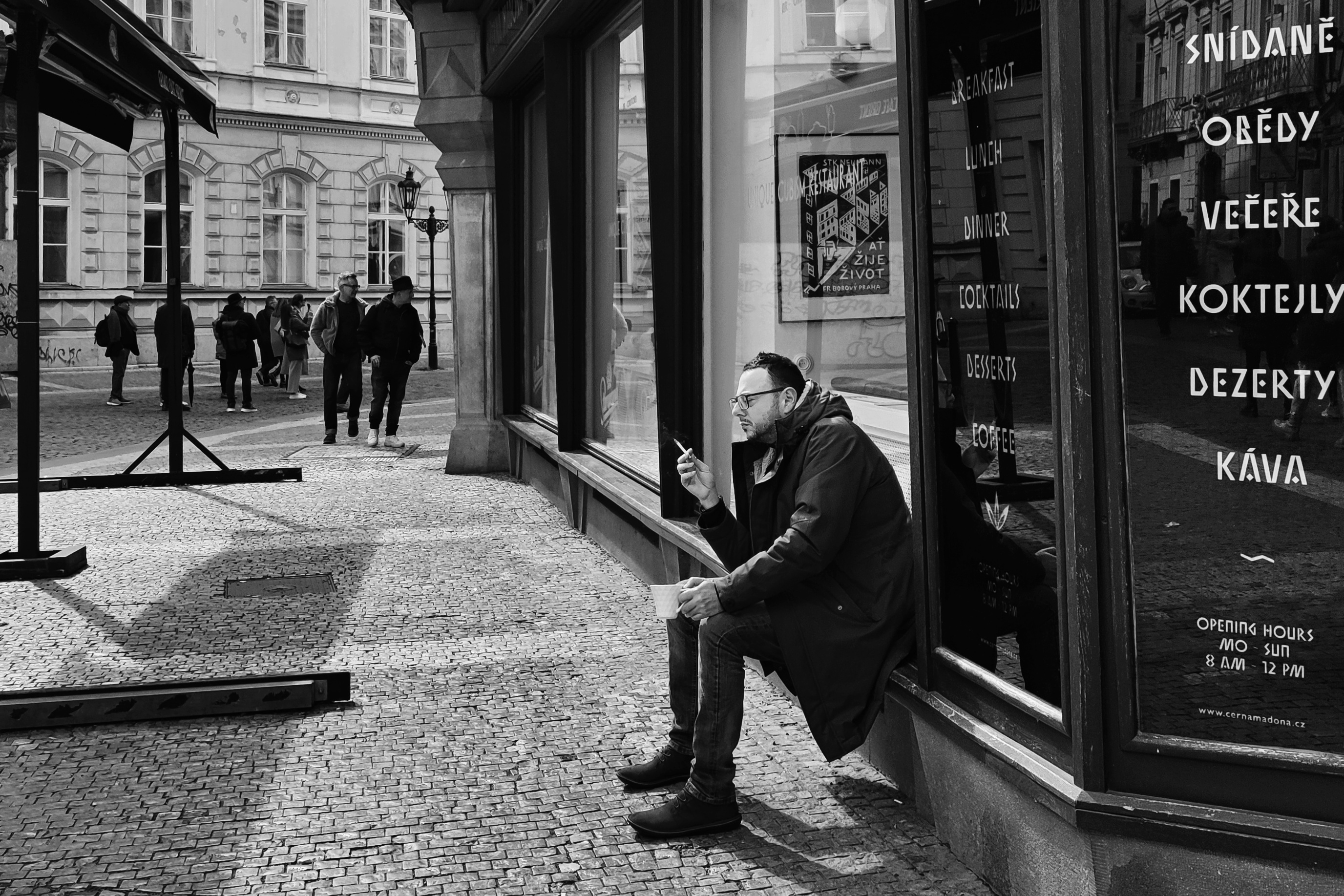muž sedí na okenním parapetu a dívá se na svůj mobilní telefon.