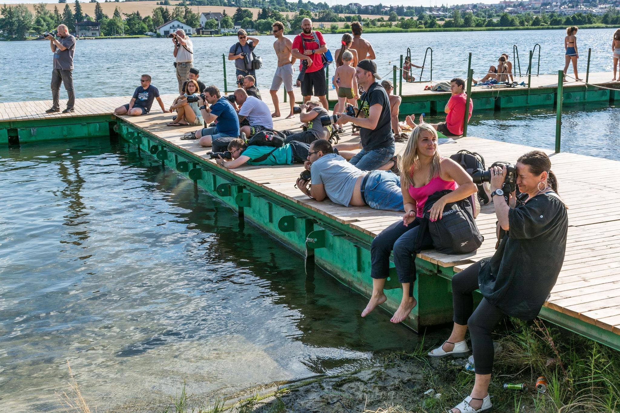 skupina lidí sedících na přístavišti vedle vodní plochy.