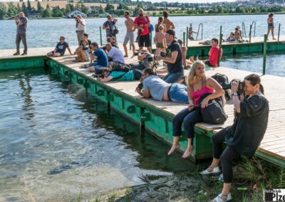 skupina lidí sedících na přístavišti vedle vodní plochy.